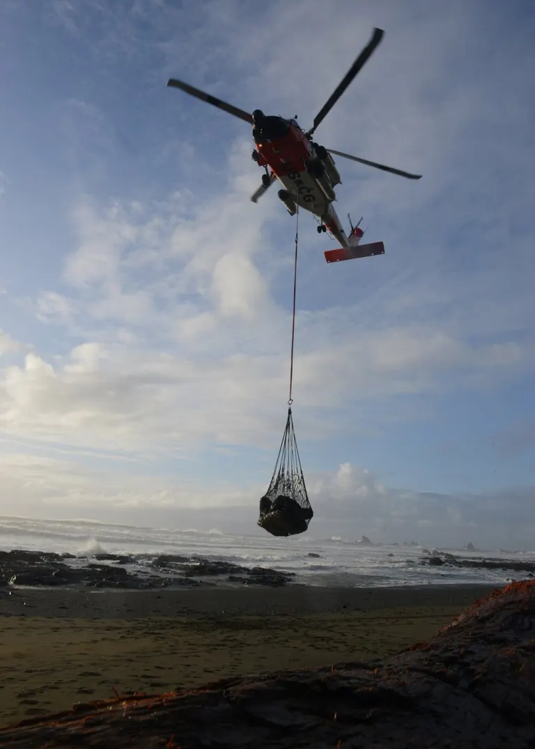A Coast Guard MH-60 Jayhawk crew lifts a net full of beach debris